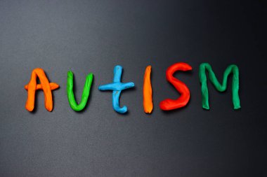 Otizm kelimesi siyah arkaplandaki renkli modelleme kilinden yapılmıştır