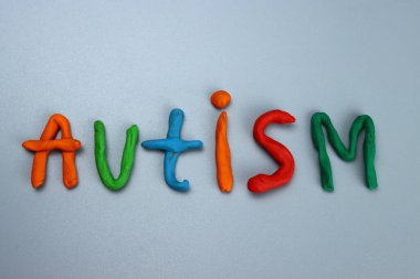 Gri arkaplandaki renkli modelleme kilinden ya da plastikten yapılmış otizm kelimesi