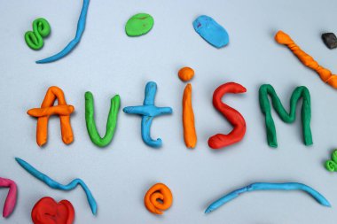 Gri arkaplandaki renkli modelleme kilinden ya da plastikten yapılmış otizm kelimesi