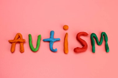 Renkli modelleme kilinden ya da pembe arka plandaki plastikten yapılmış otizm kelimesi
