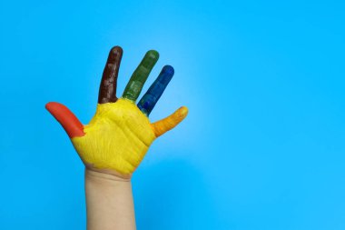 Mavi arka planda renkli boyayla boyanmış çocuk eli