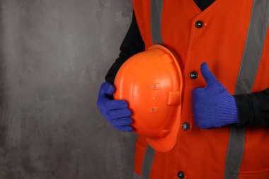 Sarı yelekli inşaat işçisi. Gri arka planda kaskı var. Eller yakın.