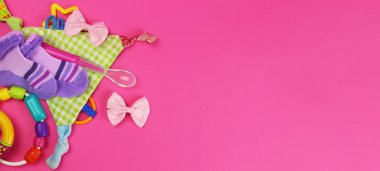 Bebek kıyafetleri, çıngıraklar, pembe arka planda beslenme kaşığı. Yatay pankart. Metin için alanı kopyala