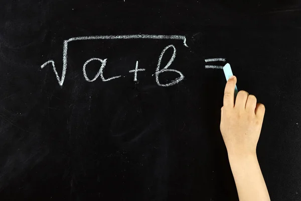 child writes a formula on a blackboard