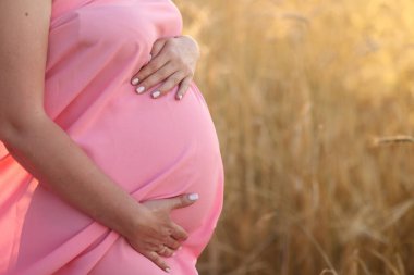 Hamile bir kadın gün batımında karnına dokunuyor.