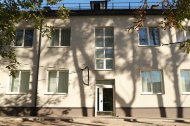 Güneşli camlar ve güçlü ağaç gölgelerinin olduğu ön cephe duvarı yıkıyor.