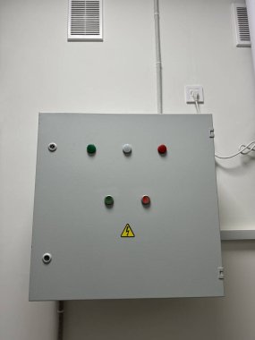 Beyaz bir duvarda elektrik kutusu. Gösterge ışıkları ve yüksek voltajlı uyarı sembolü var.