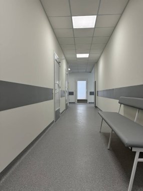 Temiz, steril hastane koridorunda boş bir bank, kapılar ve parlak ışıklandırma var.