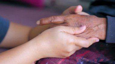 Teselli ve cesaret için yaşlı kadının ellerine dokunan genç bir kadının elleri, aile ve yaş farkı için, seçici bir odak derinliği.