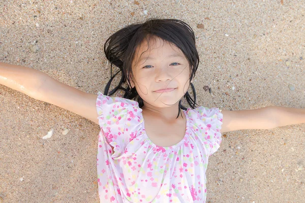亚洲微笑着可爱的小女孩躺在沙滩上的沙子。泰国志 — 图库照片