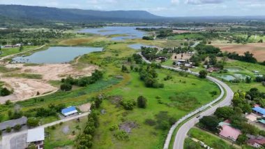 Yüksek açılı insansız hava aracı görüntüleri yeşil tarlalar ve orman tepeleriyle çevrili kırsal bir köyden geçen uzun bir otoban gösteriyor. Kırsal yaşam tarzını, ulaşım yollarını yakalıyor.