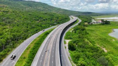 Nehir ve yeşil tepeler boyunca uzanan otobanın havadan görünüşü. Ulaşım, altyapı, seyahat ve lojistik kavramı