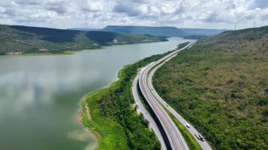 Nehir ve yeşil tepeler boyunca uzanan otobanın havadan görünüşü. Ulaşım, altyapı, seyahat ve lojistik kavramı