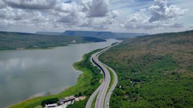 Nehir ve yeşil tepeler boyunca uzanan otobanın havadan görünüşü. Ulaşım, altyapı, seyahat ve lojistik kavramı