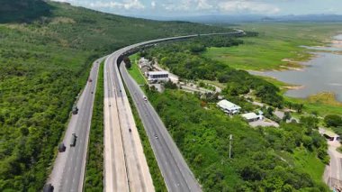 Nehir ve yeşil tepeler boyunca uzanan otobanın havadan görünüşü. Ulaşım, altyapı, seyahat ve lojistik kavramı