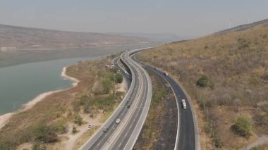 Nehir ve yeşil tepeler boyunca uzanan otobanın havadan görünüşü. Ulaşım, altyapı, seyahat ve lojistik kavramı