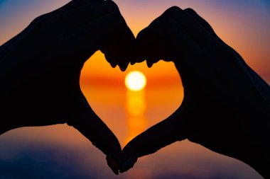 Kalp şeklinde eller arasında güzel turuncu gün batımı