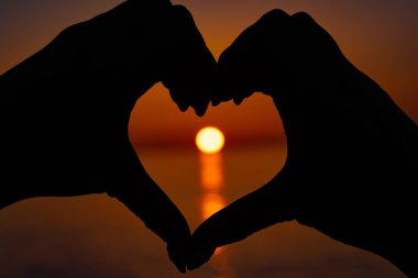Kalp şeklinde eller arasında güzel turuncu gün batımı