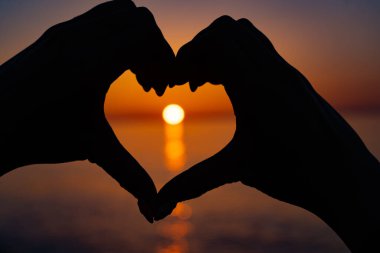 Kalp şeklinde eller arasında güzel turuncu gün batımı
