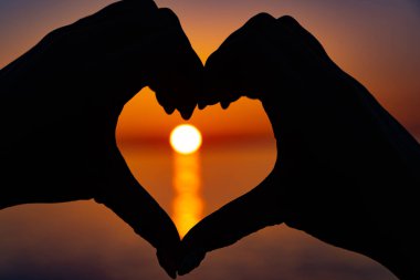 Kalp şeklinde eller arasında güzel turuncu gün batımı