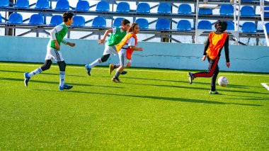 Çocuklar futbol sahasında futbol oynuyor.