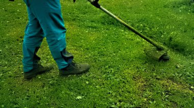 Parkta çim biçme makinesi olan bir adam çimleri temizliyor.