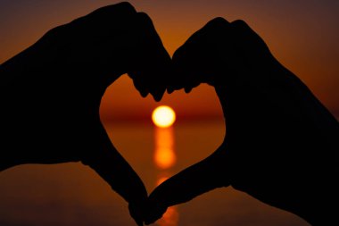 Kalp şeklinde eller arasında güzel turuncu gün batımı