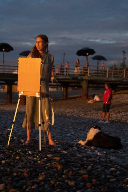 Batumi, Gürcistan - 17 Haziran 2021: Bir kız gün batımı ve denizin arka planına karşı bir resim çiziyor.