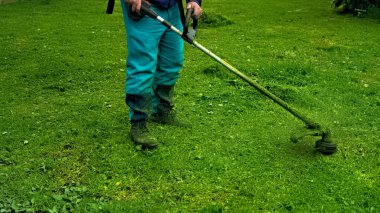 Parkta çim biçme makinesi olan bir adam çimleri temizliyor.