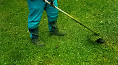 Parkta çim biçme makinesi olan bir adam çimleri temizliyor.