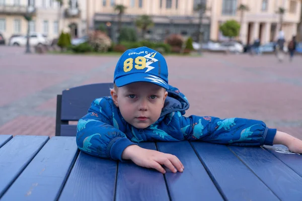 身穿蓝色帽子和蓝色夹克的男孩坐在咖啡店的桌子旁 — 图库照片