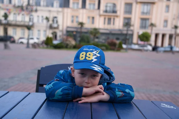 身穿蓝色帽子和蓝色夹克的男孩坐在咖啡店的桌子旁 — 图库照片