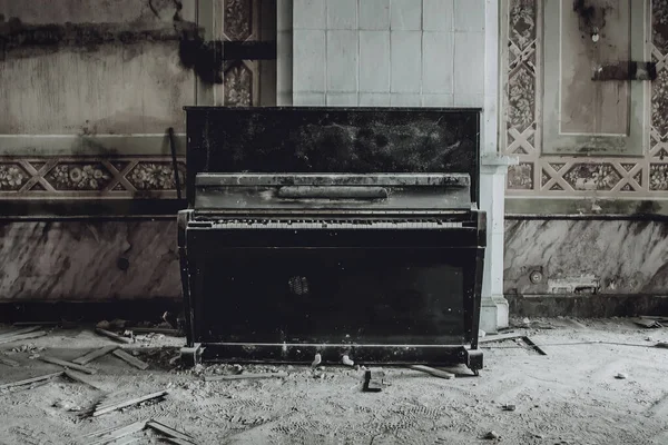 An antique black piano stands in an abandoned manor house. Shabby walls. Remains of a beautiful interior