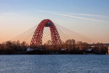 Resimli köprünün güzel demir kemeri ağaçların ve nehrin arkasından yükselir. Moskova 'da güneşli bir akşam.