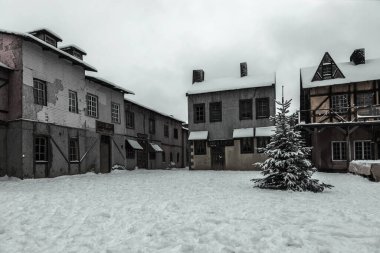 Terk edilmiş bir köyde bir meydan. Eski terk edilmiş binalar. Karda Noel ağacı. Kış soğuk bulutlu gün.