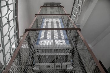 Terk edilmiş eski bir evde antika bir asansör. Merdivenler, pejmürde duvarlar. Paslı asansör boşluğu.