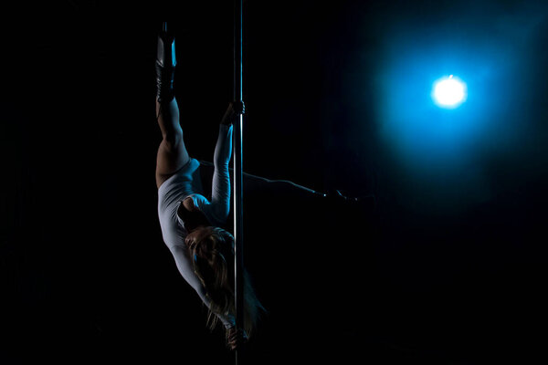 Silhouette of a girl on a pole. Aerial acrobatics. Pole dance. A beautiful dancer. Studio with a dark background. Blue Lantern. Silhouette of a beautiful girl.