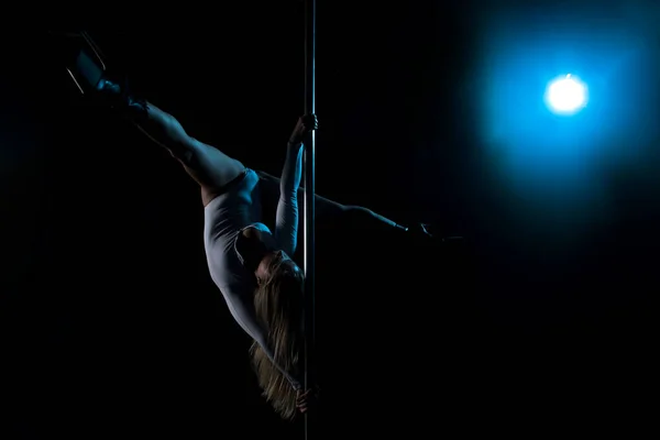 Silhouette of a girl on a pole. Aerial acrobatics. Pole dance. A beautiful dancer. Studio with a dark background. Blue Lantern. Silhouette of a beautiful girl.