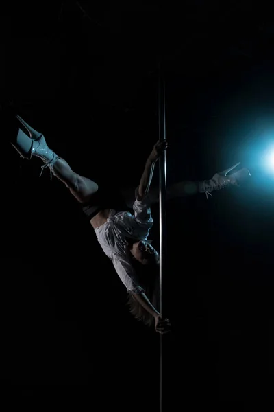 Silhouette of a girl on a pole. Aerial acrobatics. Pole dance. A beautiful dancer. Studio with a dark background. Blue Lantern. Silhouette of a beautiful girl.