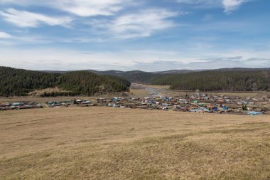Dağdan köye ve vadideki nehre güzel bir manzara. Gökyüzünde güneş ışınları. Dağların yamaçlarındaki ormanlar. Kır evleri.