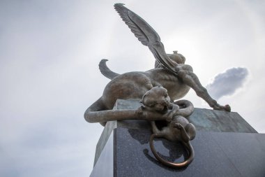 Güzel bir kız ejderha anıtına tutunuyor. Bronz heykel.