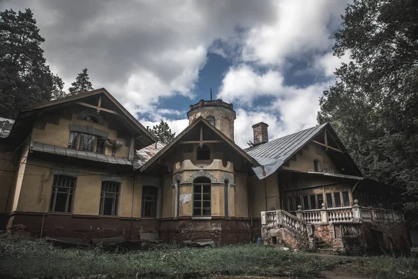 An old beautiful abandoned manor house in the forest. Blue sky with clouds. Green trees and grass. Ancient architecture of an abandoned building.