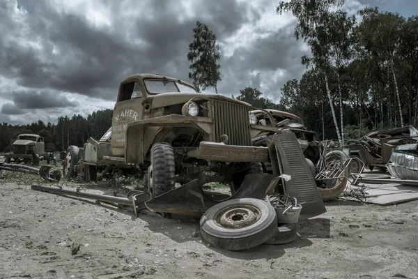 Old abandoned truck in the open air. An old abandoned car. Rusty and dirty abandoned truck. Green trees and cloudy sky.