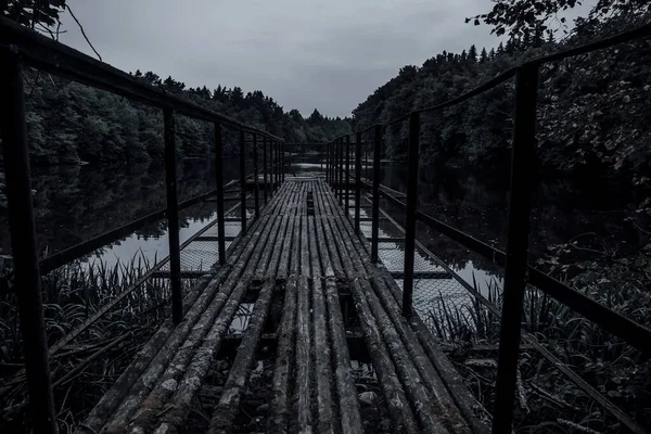 An old abandoned pier on a dark lake. Mystical landscape. Wooden, rusty and shabby dock.