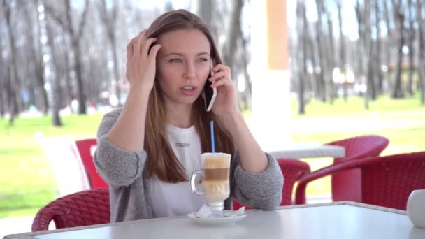 Wanita berbicara di telepon pintar minum kopi sambil tertawa di kafe. Cantik. — Stok Video