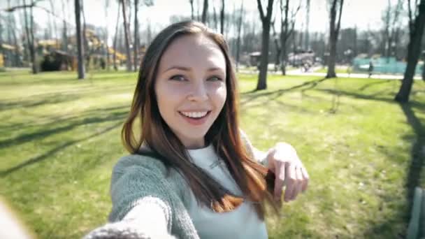 Retrato de una hermosa joven selfie en el parque con un teléfono inteligente . — Vídeo de stock