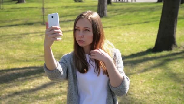 Porträtt av en vacker ung kvinna selfie i parken med en smart telefon. — Stockvideo