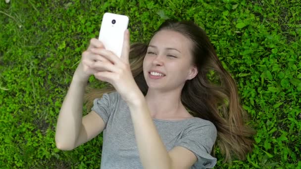 Девушка лежит на зеленом лугу на телефоне — стоковое видео