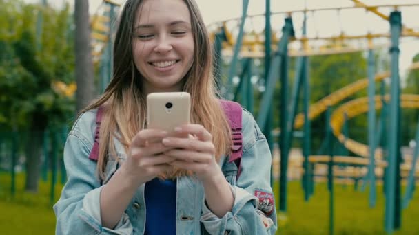 Chica con el teléfono contra el telón de fondo de un parque temático — Vídeos de Stock