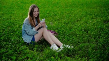 Çimenlerin üzerinde oturan genç güzel kız ve telefonda gösterir